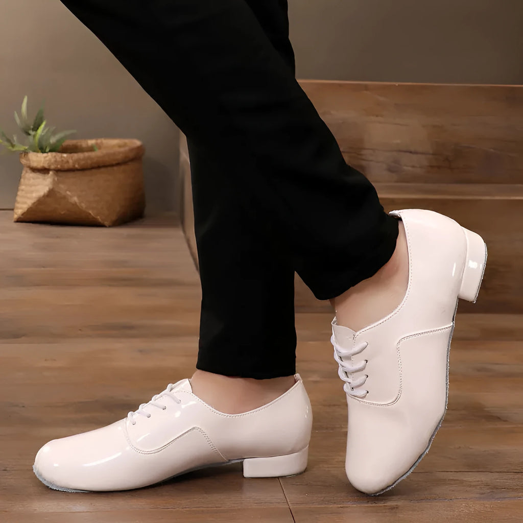 Men's black dancing shoes with a synthetic leather upper and calf leather sole, shown on a studio floor.