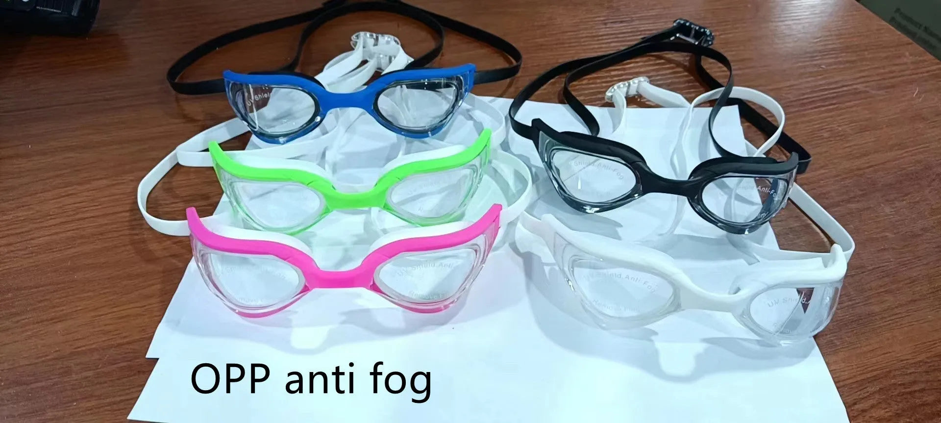 Anti-fog swimming goggles with polycarbonate lenses shown with large and small nose bridges in a plastic mirror box.