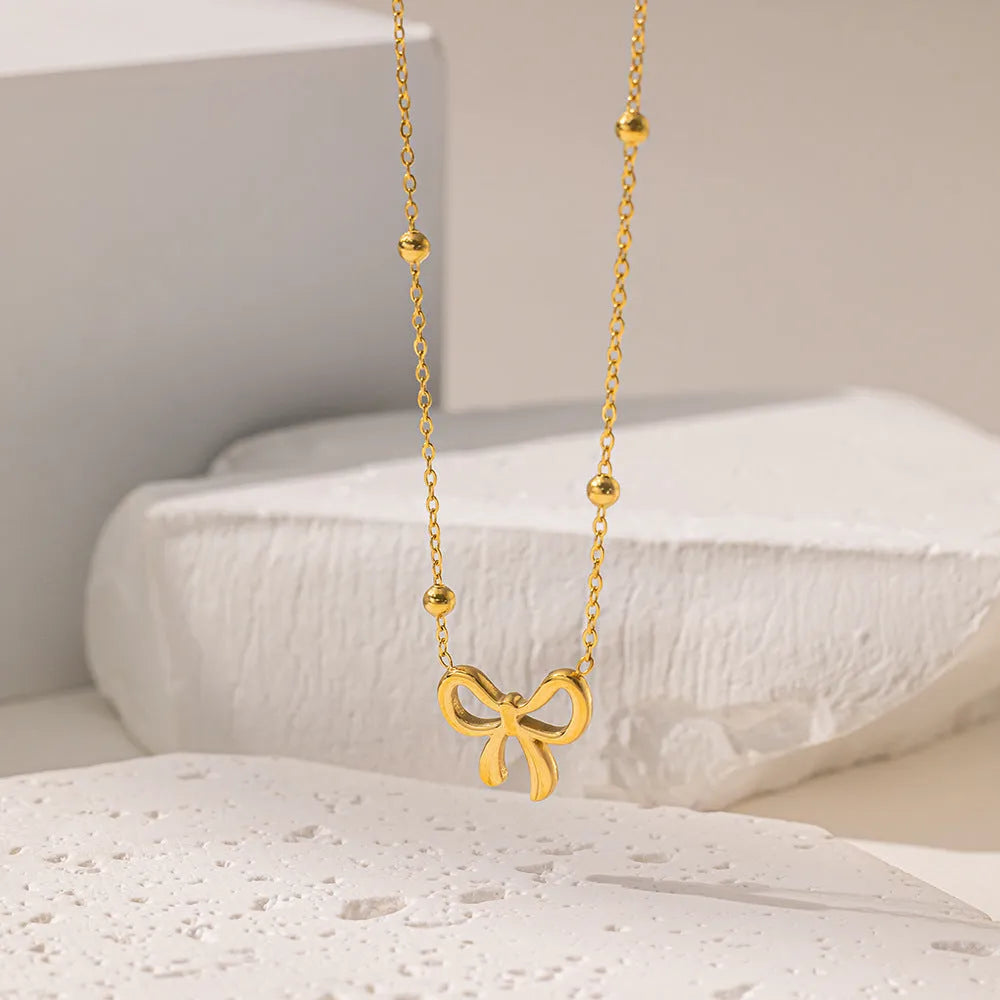 Gold electroplated bow necklace on a titanium steel cross chain, adjustable from 41 to 50 cm.