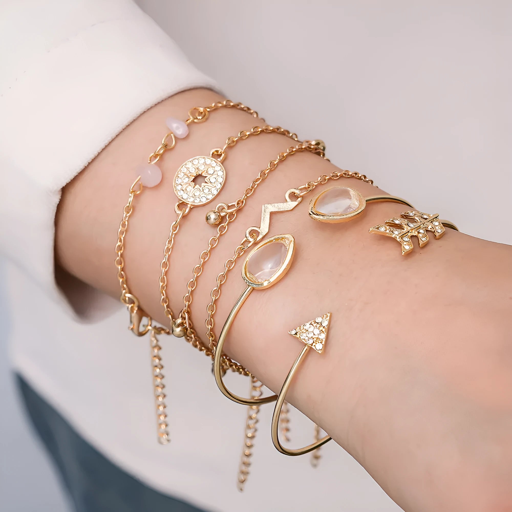 Gold-coloured six-piece women's bracelet set with arrow, water drop, and V-shaped charms on a white background.