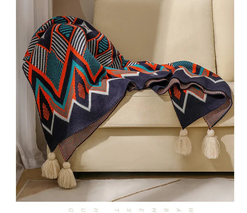 Beige and orange bohemian-style acrylic sofa blanket with tassel fringe on a grey sofa.