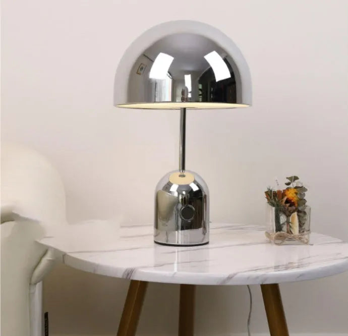 Mushroom shaped metal table lamp in rose gold finish on a wooden surface.
