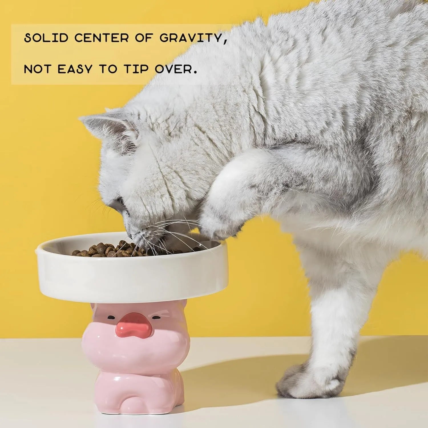 Raised ceramic cat bowl with animal design in pink, yellow, or white on a wooden floor.