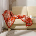 Beige and orange bohemian-style acrylic sofa blanket with tassel fringe on a grey sofa.