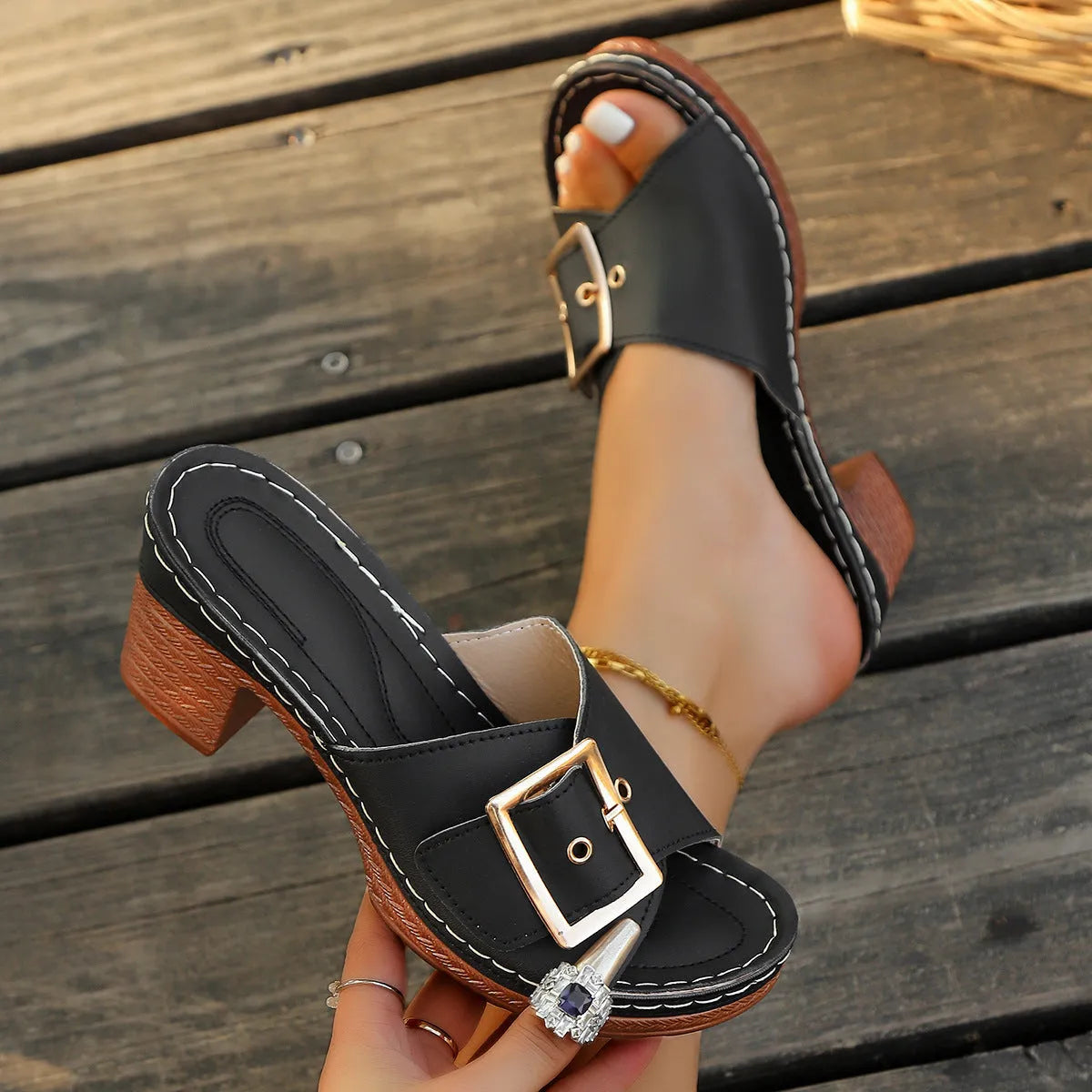 Women's black chunky heel slippers with a round toe and metal buckle on a light background.