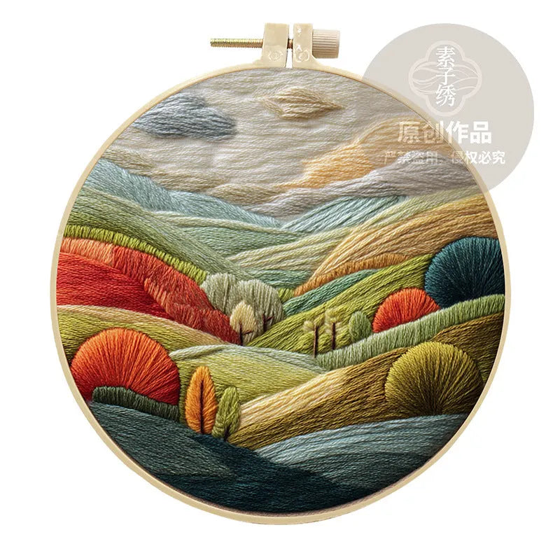 Embroidery kit with printed landscape fabric, thread, bamboo frame, and needles arranged for DIY cloth art