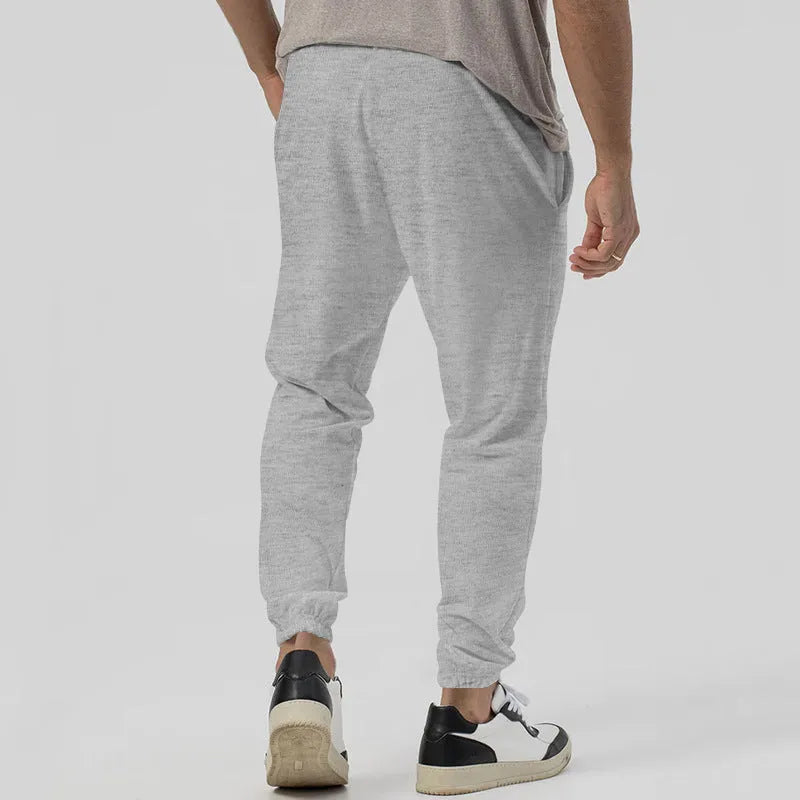 Men's grey casual tapered sweatpants with an elasticated waistband laid flat.
